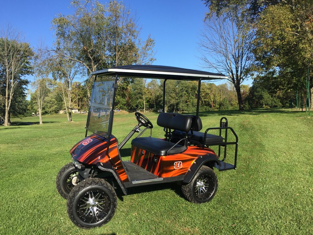 A tiger-inspired custom 2015 E-Z-GO TXT custom golf cart on a grass field during fall.